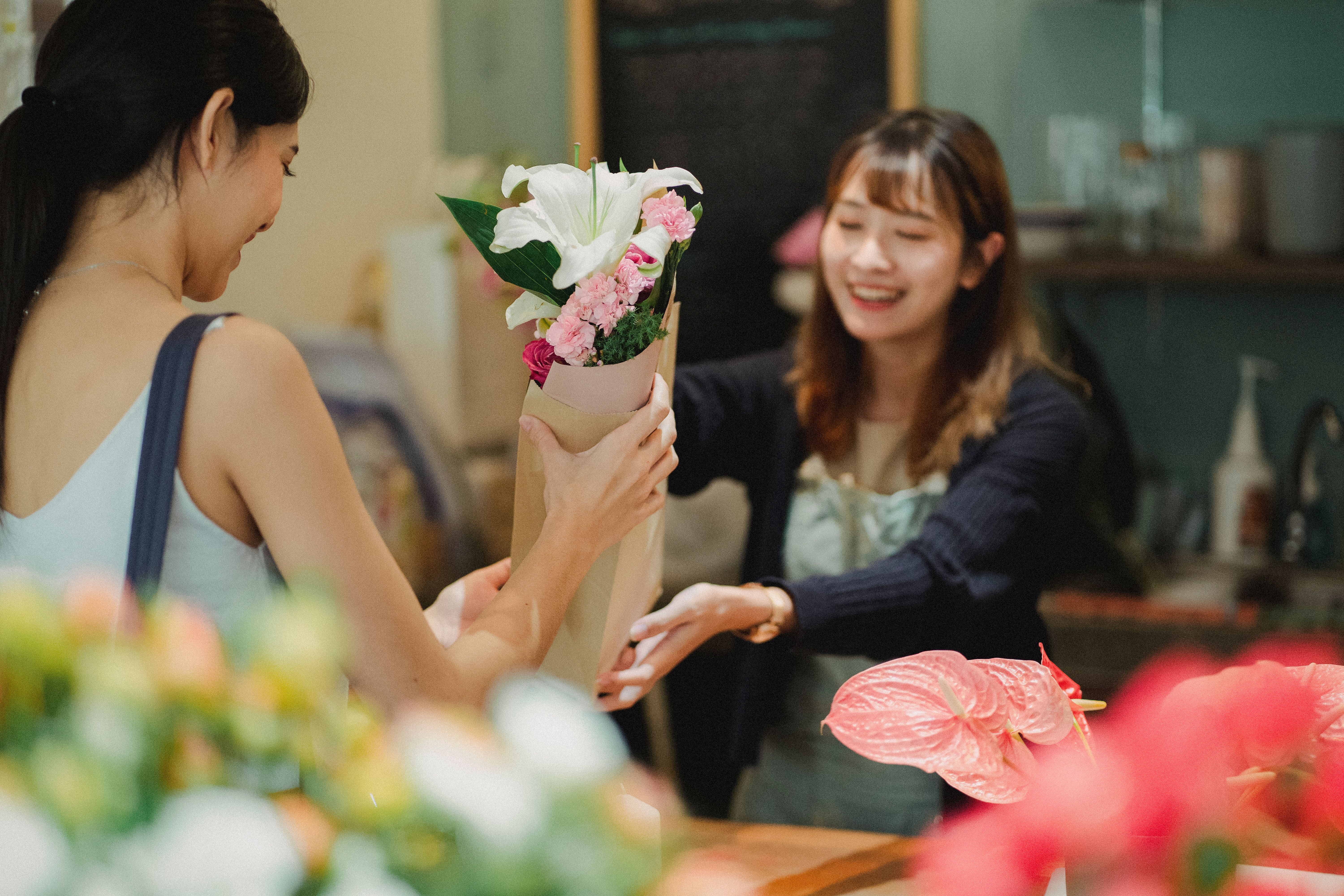 Une fleuriste remet un bouquet à une cliente dans sa boutique.