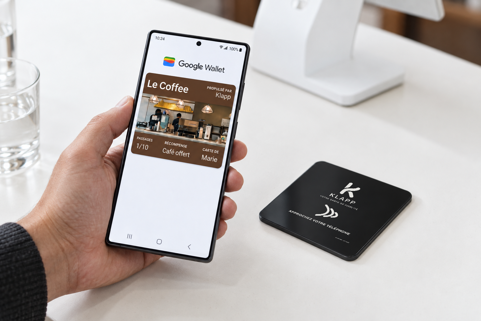 Une cliente présente sa carte de fidélité dans Google Wallet près de la plaque Klapp posée sur le comptoir.